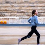 A girl runs in a historic stadium with empty stands, symbolizing youthful energy and ancient architecture.